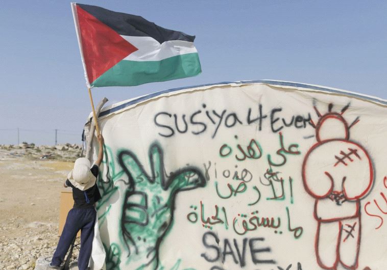 A child places a Palestinian flag on a protest tent against the demolition of the village of Susiya (Courtesy)